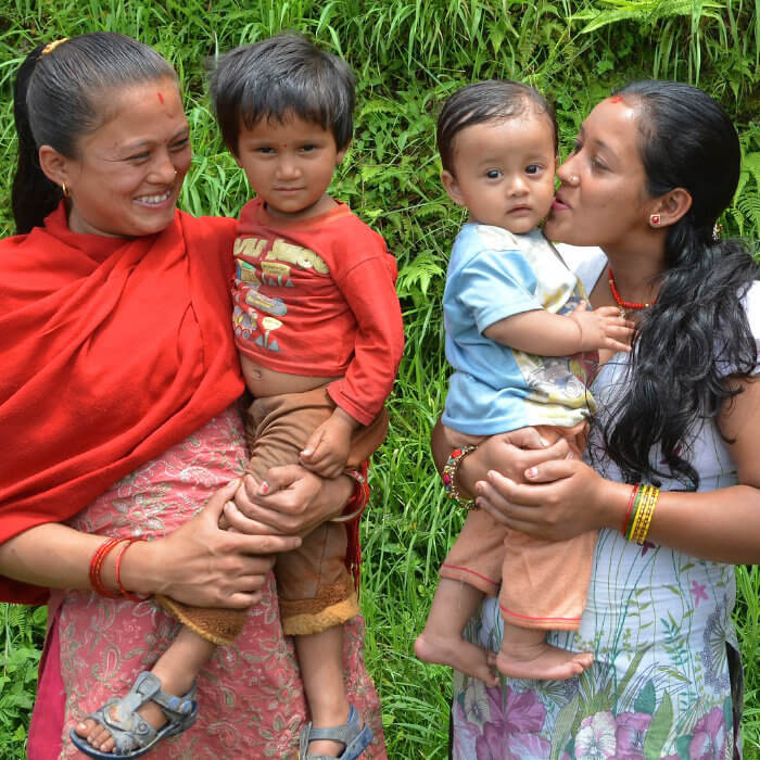 Two mothers carrying their young children smiling at the camera